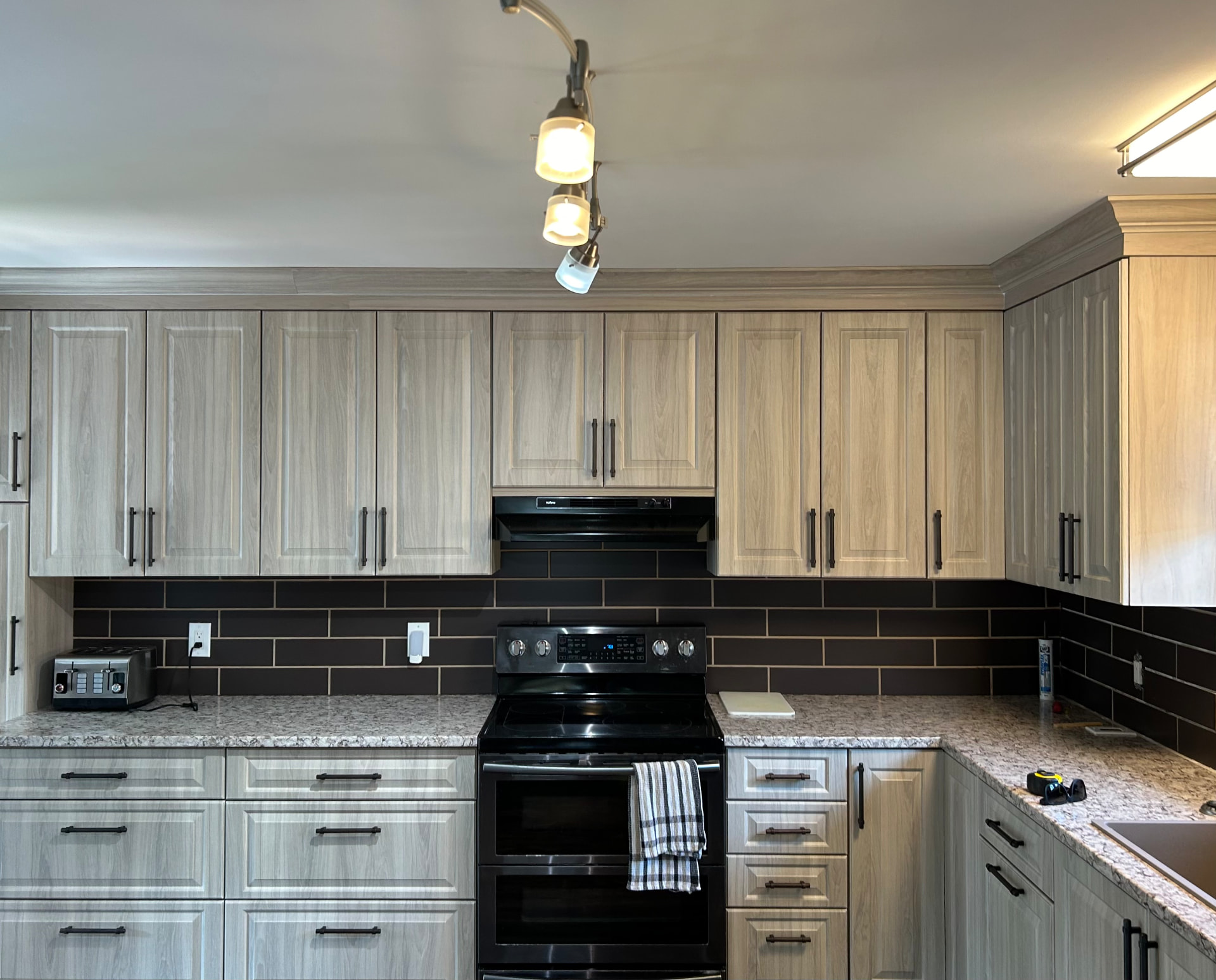 Custom greige shaker kitchen with speckled granite countertops, dark subway tile backsplash and matte black hardware